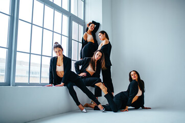 Team of five businesswoman in black suits graceful posing in white studio