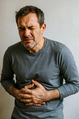 man winces with pain in stomach, human disease