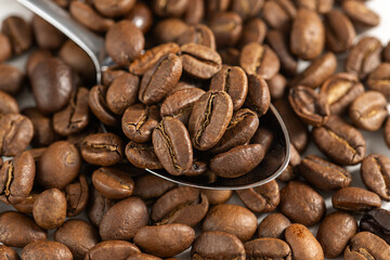 Roasted coffee beans in a spoon over bright background