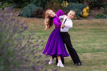 Elegant young boy and girl in ballroom dance attire performing outdoors. This juvenile dance couple...