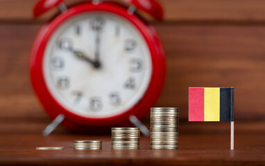 Growing money coins and Belgium flag with an alarm clock in the background. Economy, budget or...