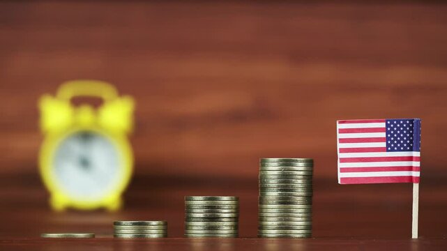 Gold money coins and american flag with an alarm clock in the background. Economy and investments concept.