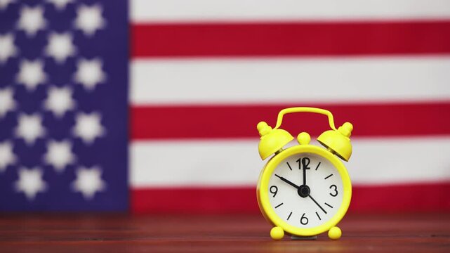 Hand puts an alarm clock with American flag in the background