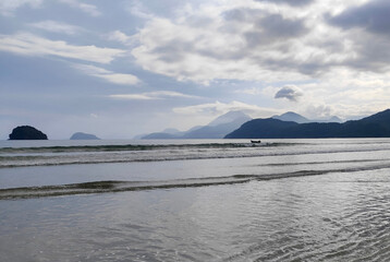 Serene beach with soft sand and calm water reflecting the sunlight. The coast is adorned by lush greenery in the background, creating an atmosphere of peace and tranquility.