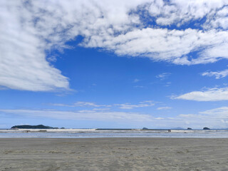 Praia da Fazenda - Ubatuba SP. A beautiful beach with fine and wavy sand, reflecting the gentle waves of the sea under a clear blue sky full of white clouds.