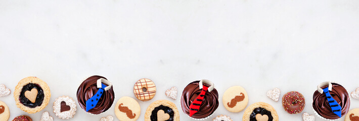 Fathers Day themed baking bottom border with assorted cookies and sweet treats. Top down view on a white marble banner background with copy space.