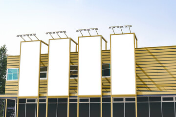 Four vertical empty white billboard mockups on the golden wall of a building.