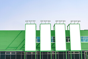 Four vertical blank white billboard mockups on the green wall of a building. Street advertising on the screen of the city.