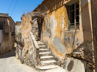Abandoned house with outside stone chairs in an alley in Gythio, Greece