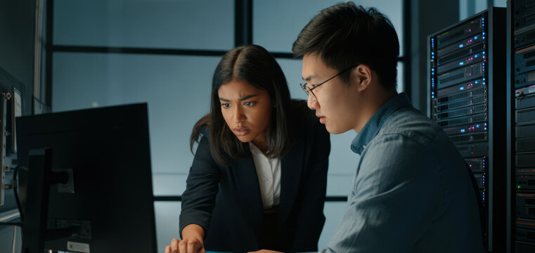 Asian male and hispanic female collaborating in server room technology setting - Powered by Adobe