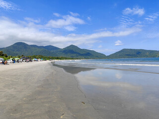 Serene beach with soft sand and calm water reflecting the sunlight. The coast is adorned by lush greenery in the background, creating an atmosphere of peace and tranquility.