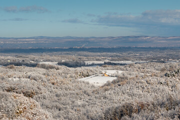 Wintry landscape of village surrounded with forest and distant hills in haze
