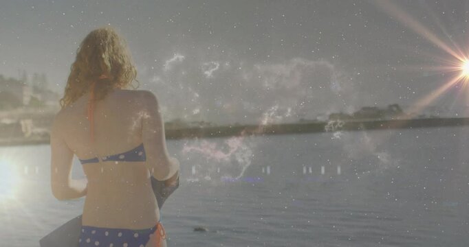 woman holding boogie board standing at water edge for travel, with cosmic sparkles and lens flare