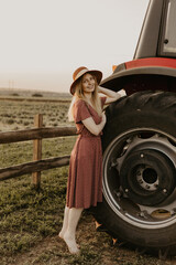 Young girl in a field near a red tractor in summer at sunset