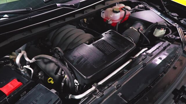 A view of the engine compartment of a modern SUV with a large spacious body. Lightly dusty black plastic covers, without manufacturer's logo. A look under the hood. View on top.
