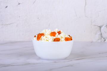 Fresh cottage cheese with dried apricot pieces in a white bowl close-up.