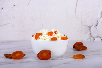 Fresh cottage cheese with dried apricots in a white cup close-up.