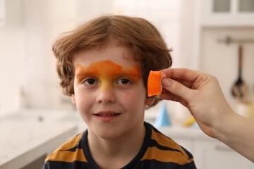 Animator drawing tiger on boy's face indoors, closeup