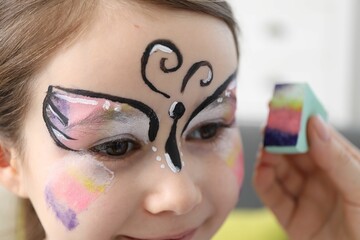 Animator drawing butterfly on girl's face indoors, closeup