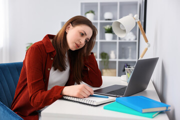 Fototapeta premium Teenage girl doing homework with laptop at table indoors