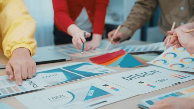 A diverse team collaborates on design concepts in a modern office, using color palettes and logo samples laid out on the table to inspire creativity and innovation. SACTR