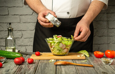 A chef mixes a vibrant salad using fresh ingredients like lettuce, radishes, cucumbers, and tomatoes, adding seasoning in a rustic kitchen environment