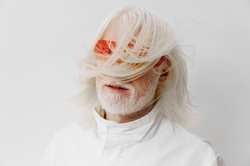 Stylish senior man with long white hair and orange sunglasses against a minimalist white...