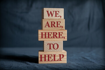 Stacked wooden blocks display the message "We are here to help", conveying support and assistance, ideal for customer service or community support initiatives