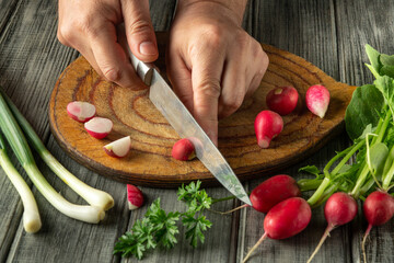 Hands skillfully slice vibrant radishes on a wooden board, surrounded by fresh greens and herbs, capturing the essence of healthy cooking in a warm kitchen atmosphere