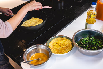 Hands of woman preparing kimbap with bowls and plates of colorful fresh ingredients on white kitchen counter