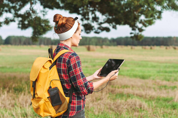 A girl with a yellow backpack in her pocket is charging a power bank, holding a tablet in her...