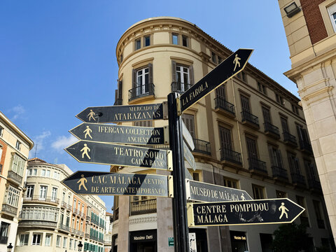 Street signs and landmark directions in Malaga, Spain under a sunny sky