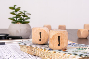 Exclamation marks on wooden cubes with cash and data sheet.