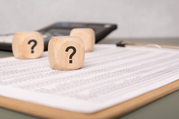 Wooden block with question mark on financial document, symbolizing uncertainty