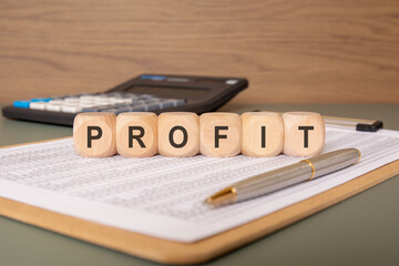 wooden cubes spelling PROFIT on a financial sheet with pen and calculator