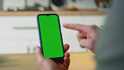 Hand pointing smartphone green screen browsing application in apartment closeup.