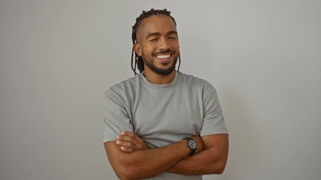 Young smiling man with braids stands confidently with arms crossed against a plain white background exuding charisma and style.