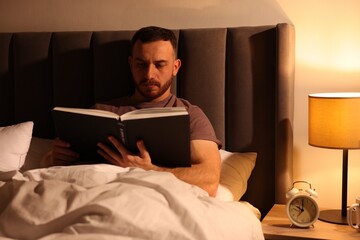 Young man reading book in bed at home