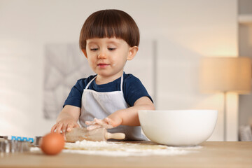 Cute little boy shaping dough with rolling pin at table indoors