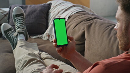 Obraz premium Guy browsing greenscreen cellphone relaxing on couch home closeup. Relaxed man