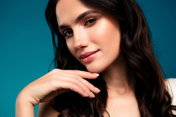 Tempting young woman with flawless makeup and brunette hair posing against a blue studio background