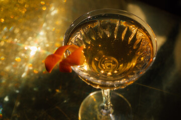 cocktail in coupe glass with orange twist on sparkling golden background, table