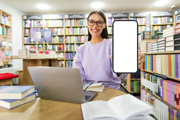 Mockup for educational app. Lady student sitting at table in library, showing her smartphone with...