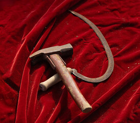 Closeup of a vintage hammer and sickle dark red velvet fabric. The tools, historically symbolic of...