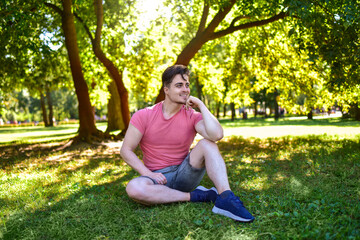 Happy Young Man Looking Away Sitting in Sunny Park