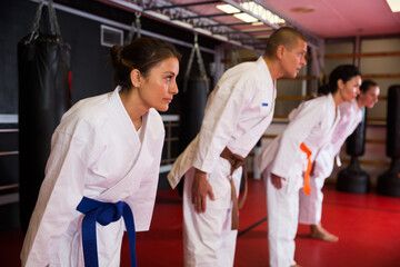 Group of people in kimono bowing during karate training in gym.