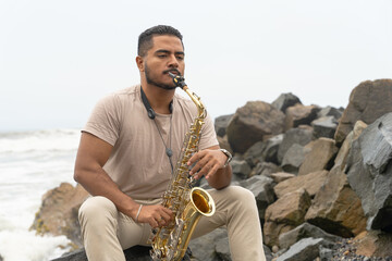 Saxophonist playing sax on a rocky beach seeking inspiration