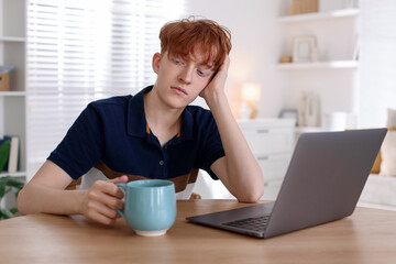 Teen problems. Depressed teenage boy with drink and laptop at desk indoors