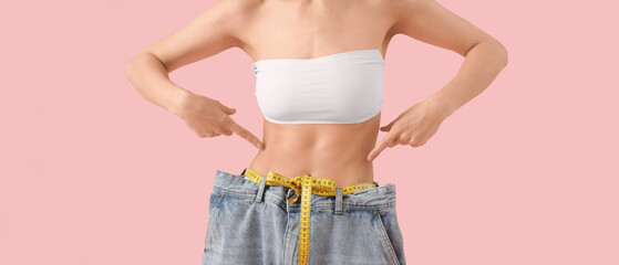 Beautiful young woman with measuring tape wearing loose jeans on pink background, closeup. Weight...