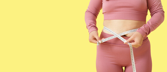 Overweight young woman with measuring tape on yellow background, closeup. Weight gain concept